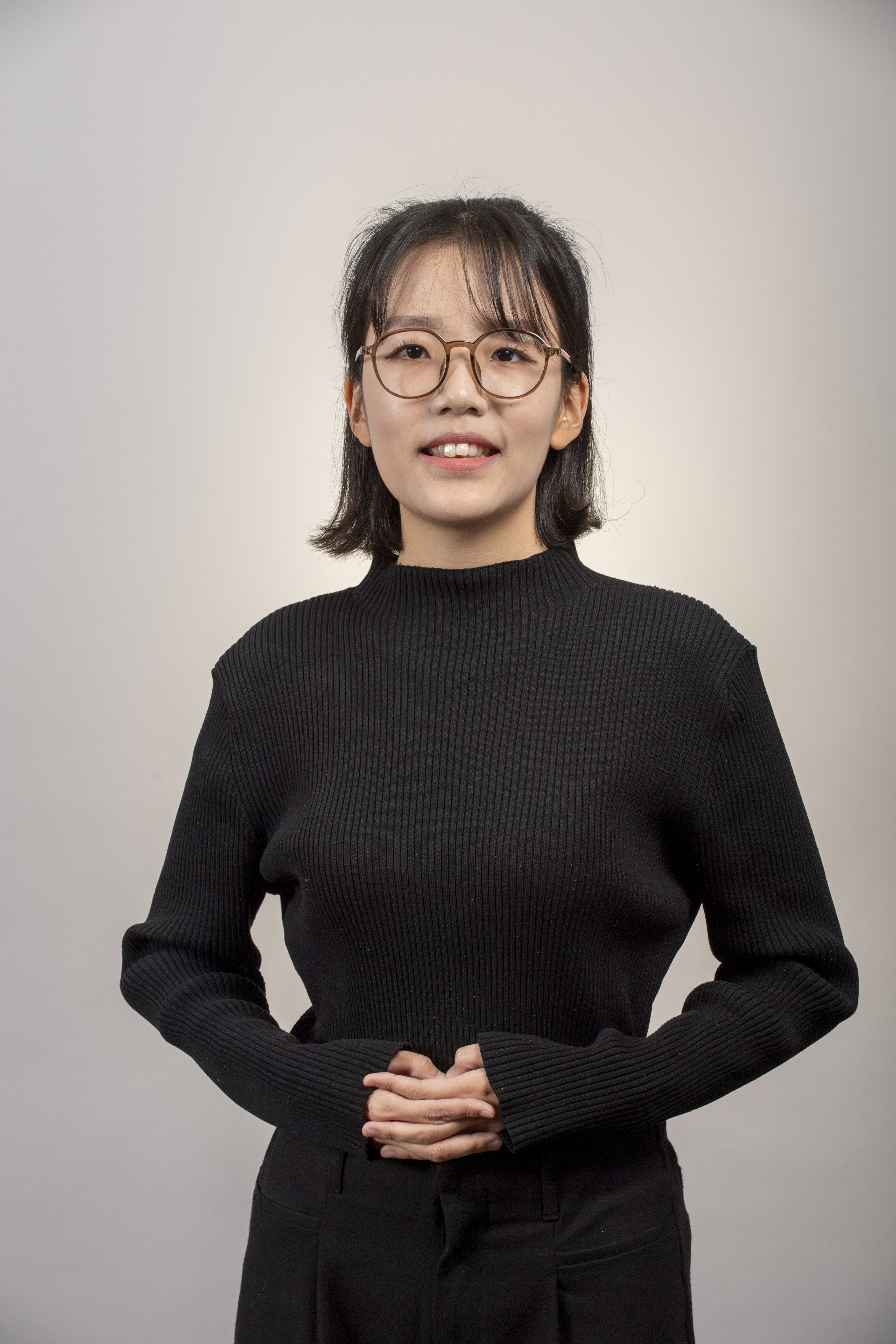 photo of Heerak Choi, a young Korean woman with short black hair wearing bllack pants and a black turtleneck sweater. She is wearing glasses