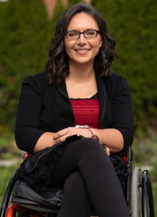 photo of Marjorie Aunos, a young white woman in a black suit with a red top sitting in a wheelchair.