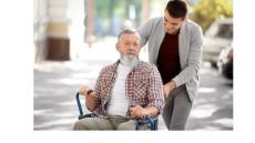 photo of an older white man in a wheelchair with a younger white man leaning over him to talk