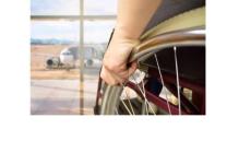 a photo of a hand holding the wheel of a wheelchair facing a window that looks out at an airplane on the tarmac