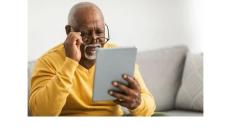 a photo of an older Black man in a yellow sweater looking at a digital tablet