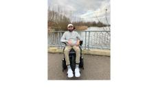 color photo of Viraj, a young man of Indian descent, sitting in a wheelchair outdoors on a bridge with a stream below.