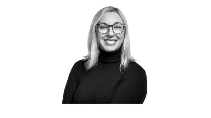 a black and white photo of Kelly Keel, a young white woman with blonde straight hair and glasses wearing a black turtleneck