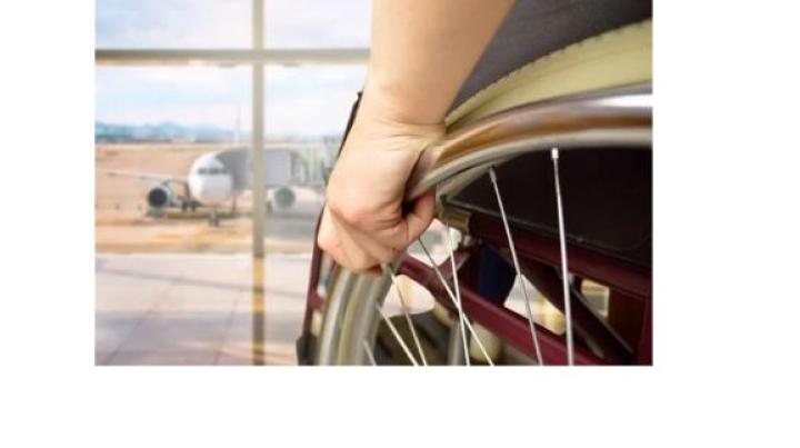 a photo of a hand holding the wheel of a wheelchair facing a window that looks out at an airplane on the tarmac