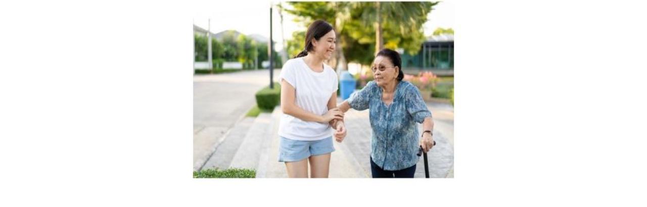 a photo of a young asian woman in blue shorts and a white t shirt helping an older Asian woman in a blue blouse and black pants with a cane