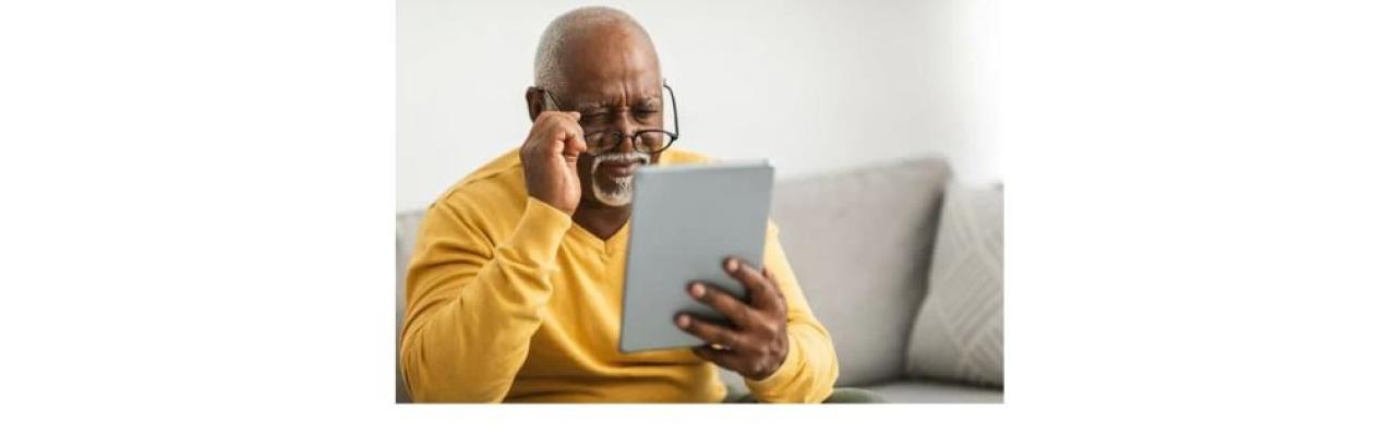 a photo of an older Black man in a yellow sweater looking at a digital tablet