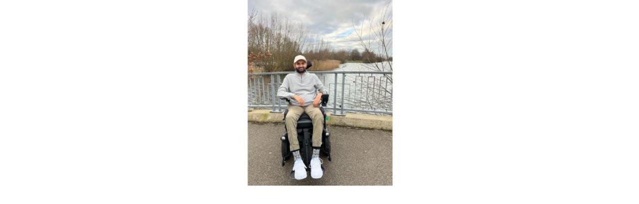 color photo of Viraj, a young man of Indian descent, sitting in a wheelchair outdoors on a bridge with a stream below.