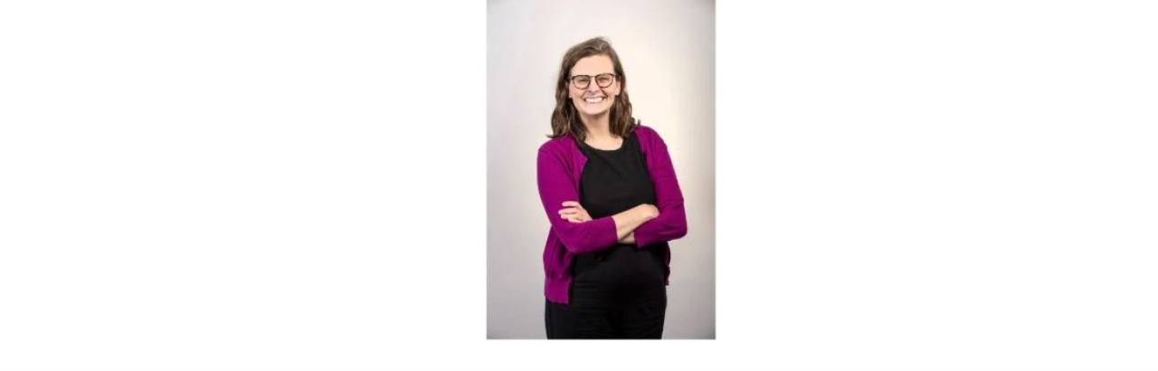 photo of Amy McArthur, a young white woman with long brown hair and glasses wearing a pink top and black pants