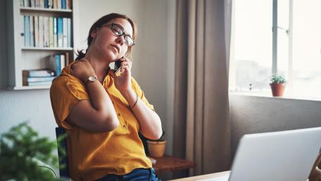 woman rubs her neck while sitting in a home office