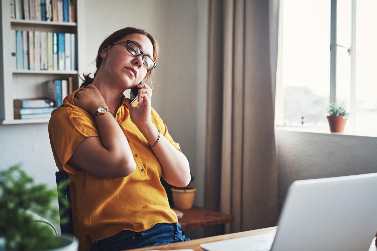 woman rubs her neck while sitting in a home office