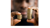 A black man is holding two stacks of gold coins in each hand. The stack of coins in the left hand is smaller than the stack of coins in the right hand. 