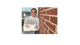 Niveda - young woman in white turtleneck smiling and leaning against a brick wall