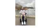 color photo of Viraj, a young man of Indian descent, sitting in a wheelchair outdoors on a bridge with a stream below.